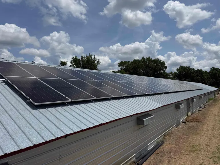 Solar panels mounted flush along the metal roof of an agricultural building against a cloudy sky