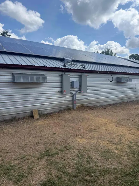 End view of an agricultural building showing roof-mounted solar panels above wall-mounted electrical equipment