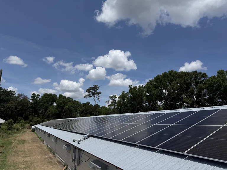 Solar panels along the roof of an agricultural building with ventilation fans visible in the sidewall below