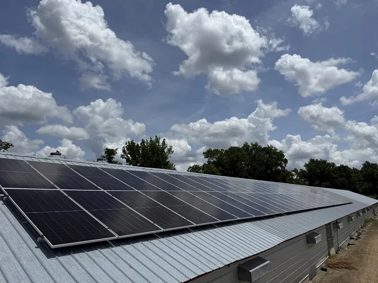 View from the ridge of an agricultural building looking down a long run of roof-mounted solar panels under a cloudy sky