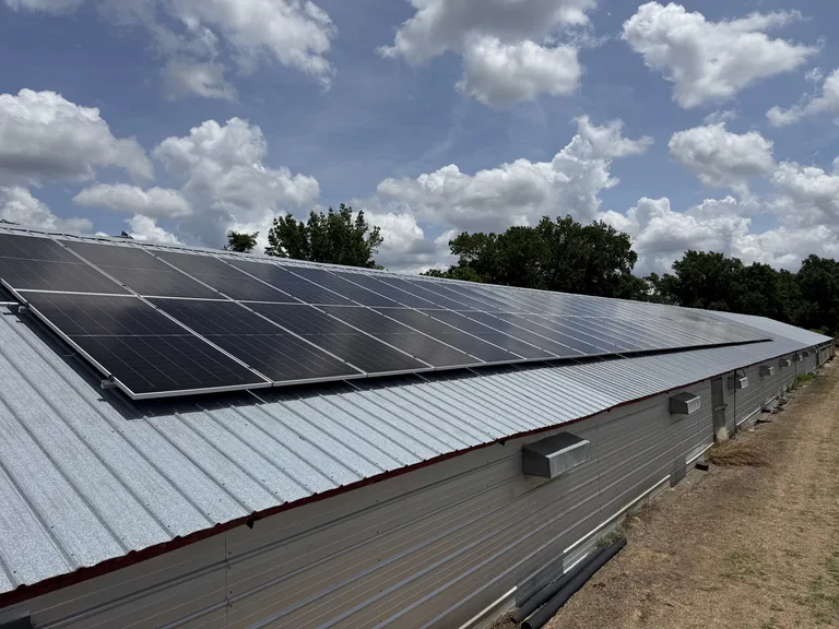 Close view of roof-mounted solar panels above the corrugated metal wall and vent boxes of an agricultural building