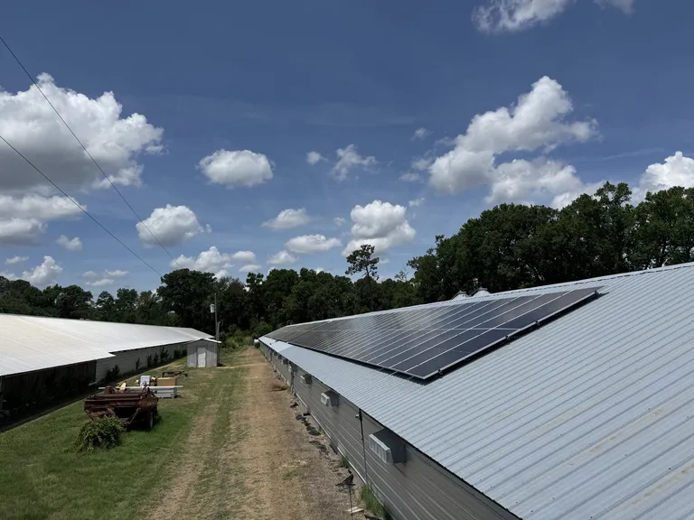 Two parallel agricultural buildings with a track between them, solar panels on the roof of one and bare metal on the other