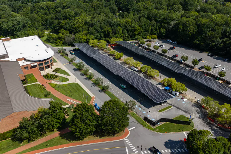 Solar canopies over a parking lot with campus lawn and buildings behind