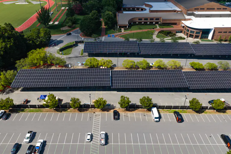 Parallel solar canopy rows over campus parking with buildings behind