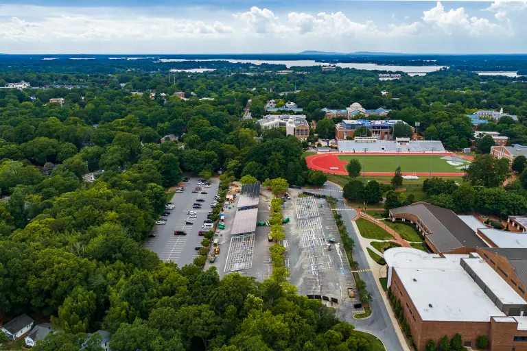 Wide aerial of the Davidson College campus during solar canopy construction, with the lake on the horizon