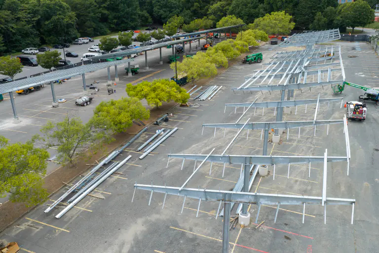 Bare steel canopy framework under construction over a campus parking lot