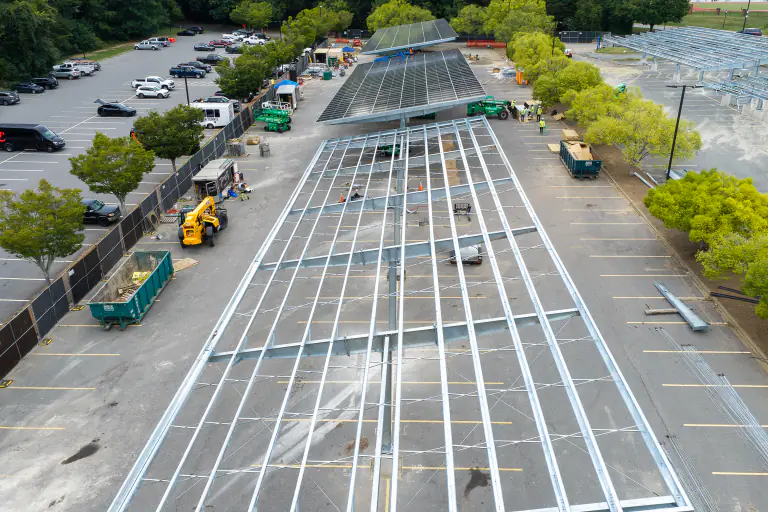 Aerial view along an unfinished steel canopy row with construction lifts alongside
