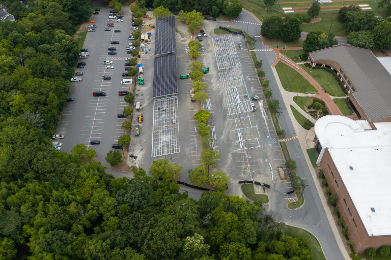 Wide aerial of the parking lots during canopy construction with woods surrounding